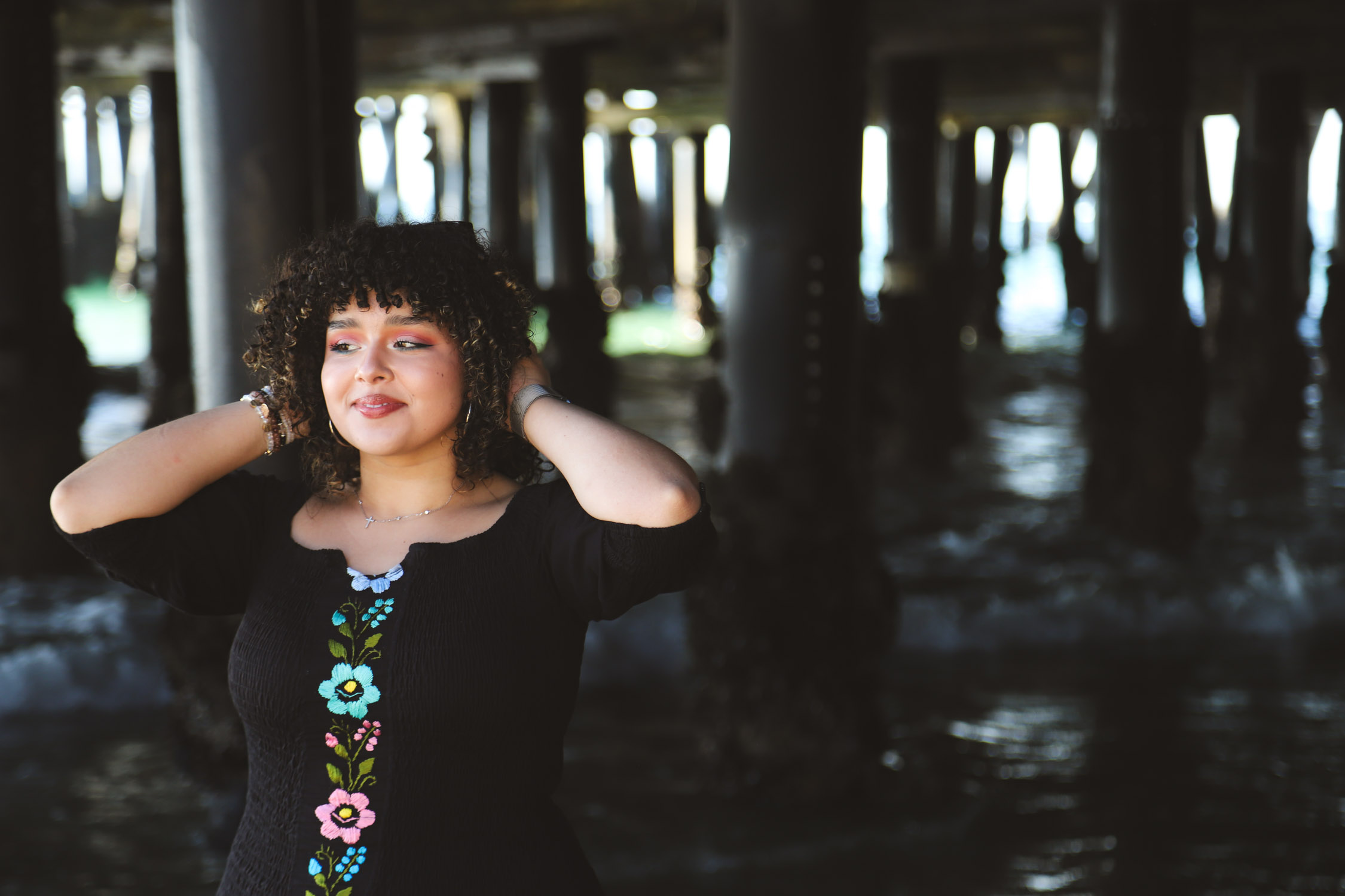 AJ posing and holding her hair under a pier at the beach